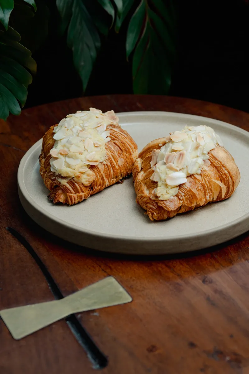 Two almond croissants, flaked and dusted, on a stone plate.