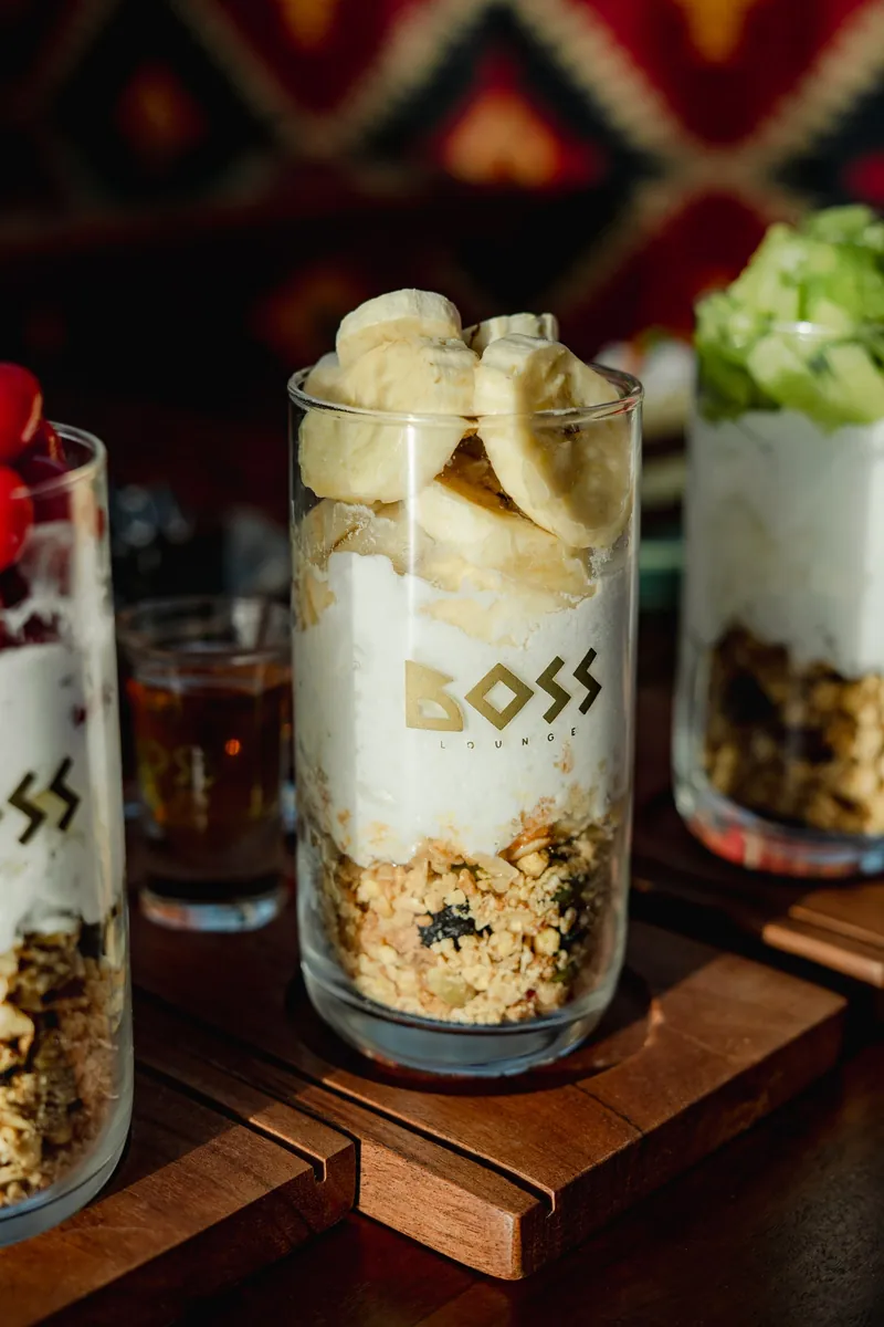 A yoghurt and granola parfait in a BOSS glass, sliced banana stacked on top.