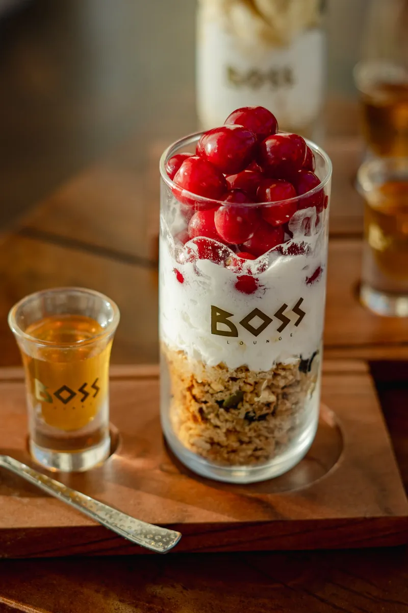 A layered yoghurt and granola parfait in a BOSS glass, cherries piled on top.