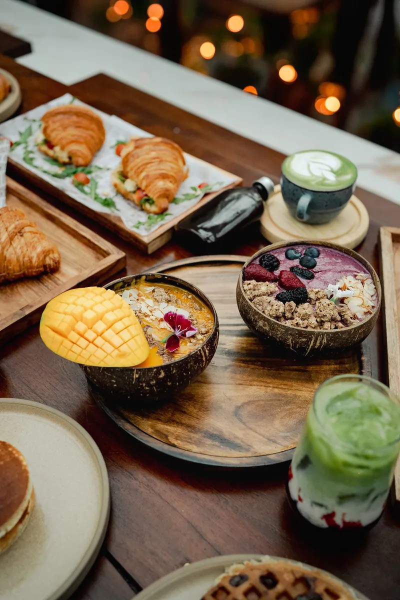 Coconut bowls of fruit and granola beside a plate of waffles and a scored mango.