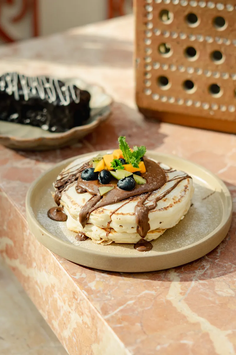 Pancakes under a chocolate drizzle, topped with mango and blueberries.