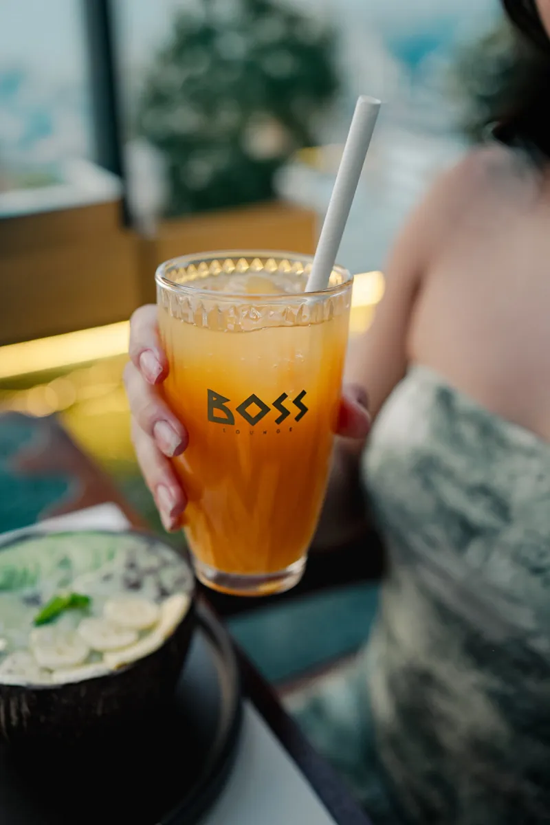 A citrus cooler in a BOSS glass with a straw, held against a red dress.
