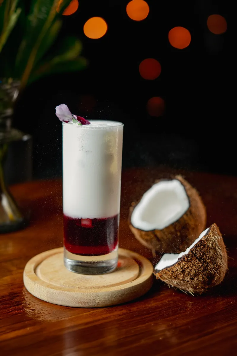 A layered coconut cooler in a tall glass beside a split coconut.
