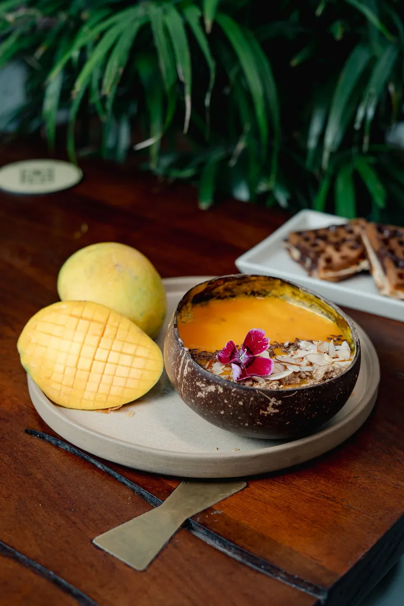A mango bowl served in a coconut shell with a flower, a scored mango beside it.