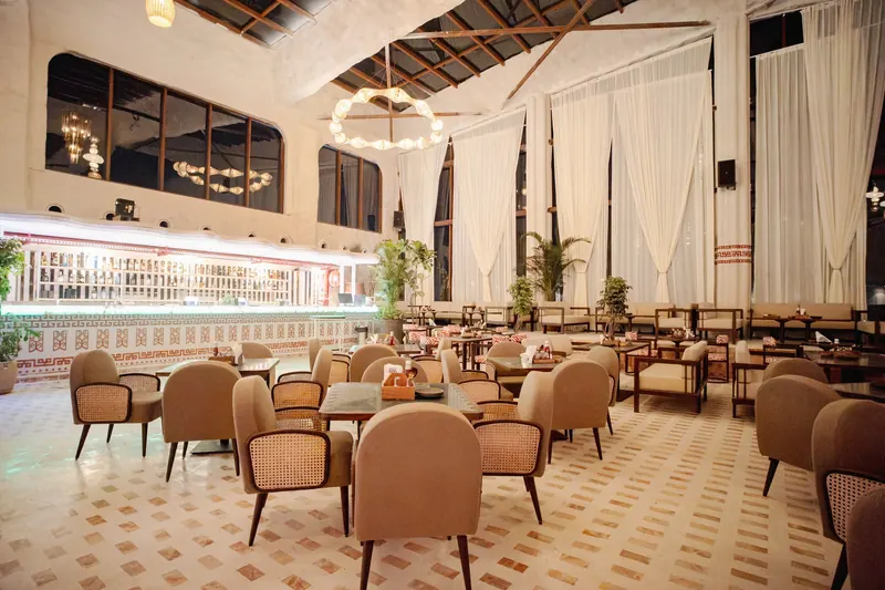 The bar at BOSS, its bottle wall lit end to end behind the counter, cane chairs and tall drape-hung windows in front.