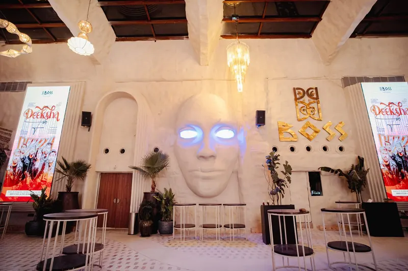 The sculpted face on the BOSS wall, its eyes lit blue, the gold BOSS wordmark beside it between two event posters.