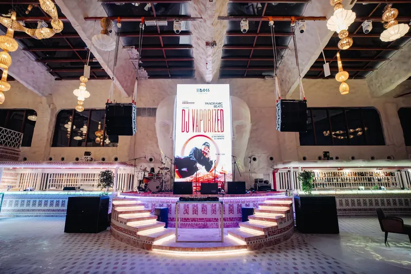 The DJ booth on the curved stage, a performance poster on the screen behind it and speaker stacks either side of the empty floor.
