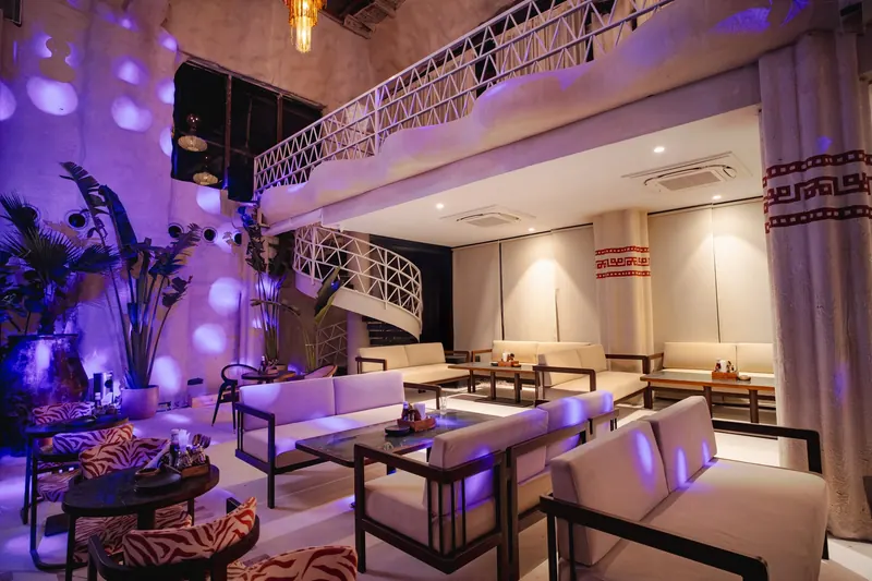 The mezzanine lounge after midnight, the spiral stair and the plants around it washed in purple.