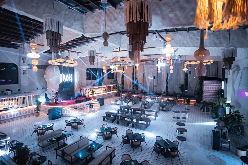 The floor at night under blue light, the BOSS sign glowing above the bar and tasselled chandeliers overhead.
