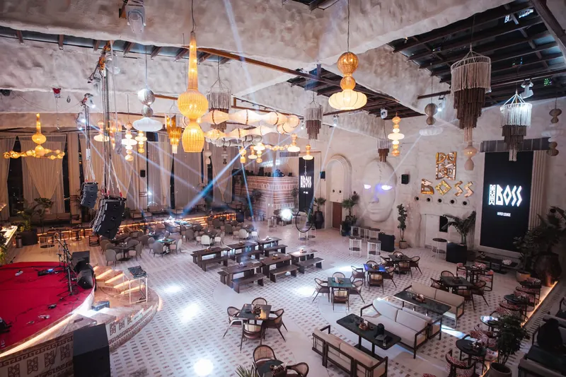The room at full tilt: warm gold light over the tables, the sculpted face and gold BOSS wordmark lit on the right, the stage red on the left.